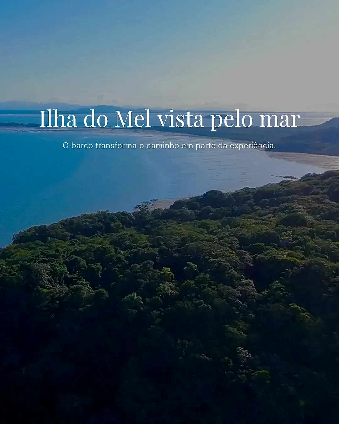 Vista aérea da Ilha do Mel, com mata densa em primeiro plano, faixa de praia e mar calmo ao fundo. A luz suave do dia cria tons azulados na água e destaca o relevo da costa.