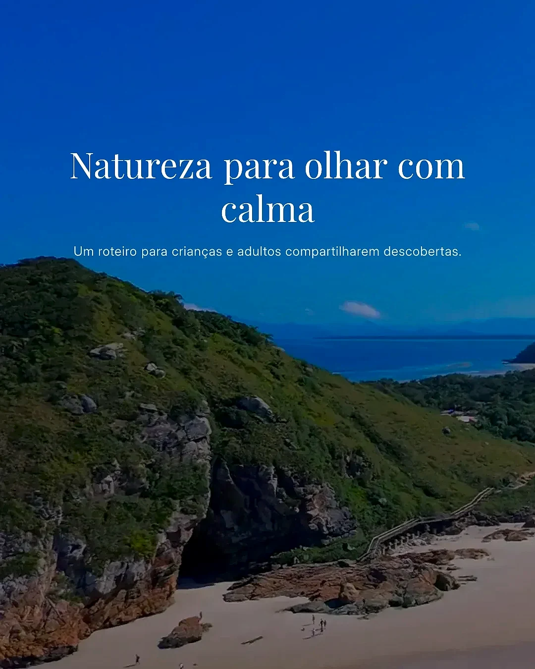 Vista aérea de praia com faixa de areia, formações rochosas e morro coberto por mata, atravessado por uma trilha de madeira. Pequenas pessoas aparecem na areia sob luz diurna intensa e céu azul.