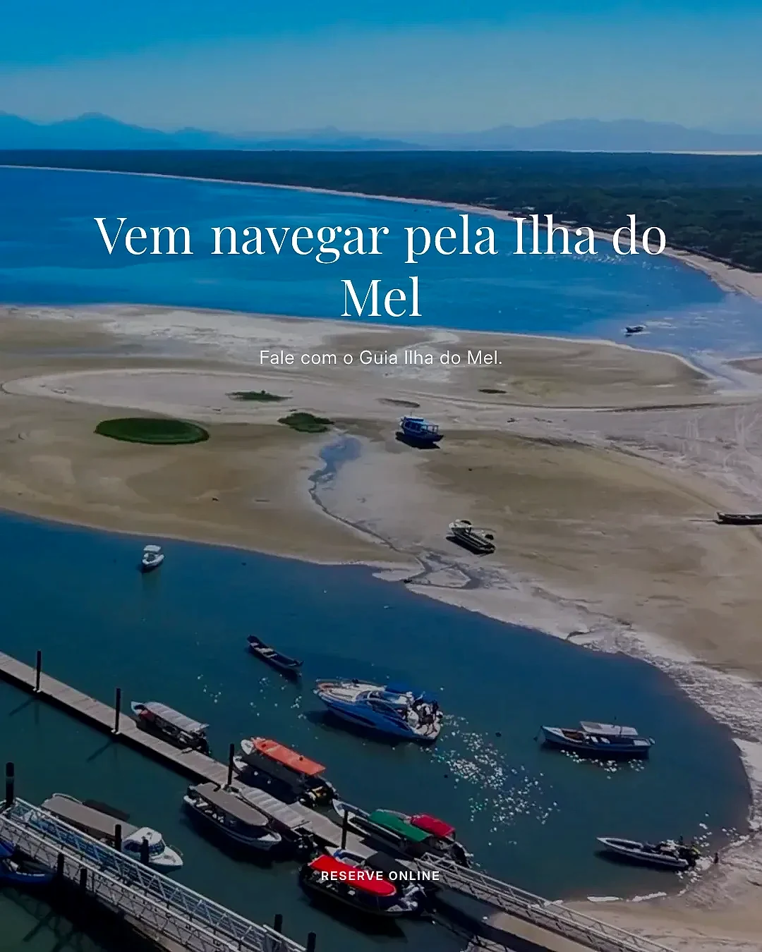 Vista aérea de um trapiche com barcos atracados junto a bancos de areia e um canal de águas calmas, cercados por faixa de praia e mata ao fundo. A cena é iluminada por luz diurna intensa, com tons azuis predominantes.